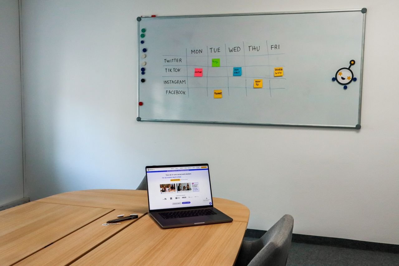 gallery-5 Office setup featuring a conference table, laptop, and organized whiteboard schedule, highlighting a tech-driven workspace.