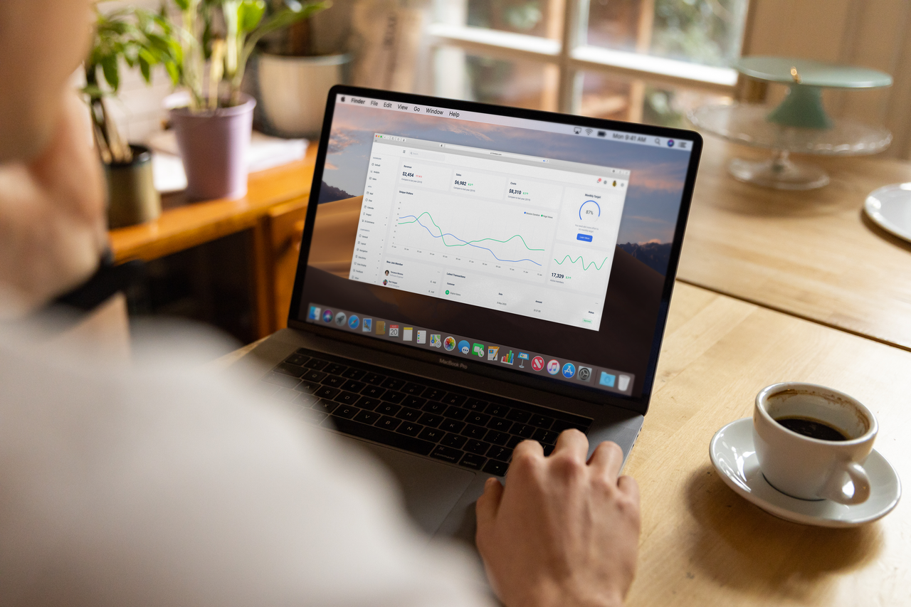 gallery-2 Person analyzing stock market data on laptop indoors with a casual setting and coffee.