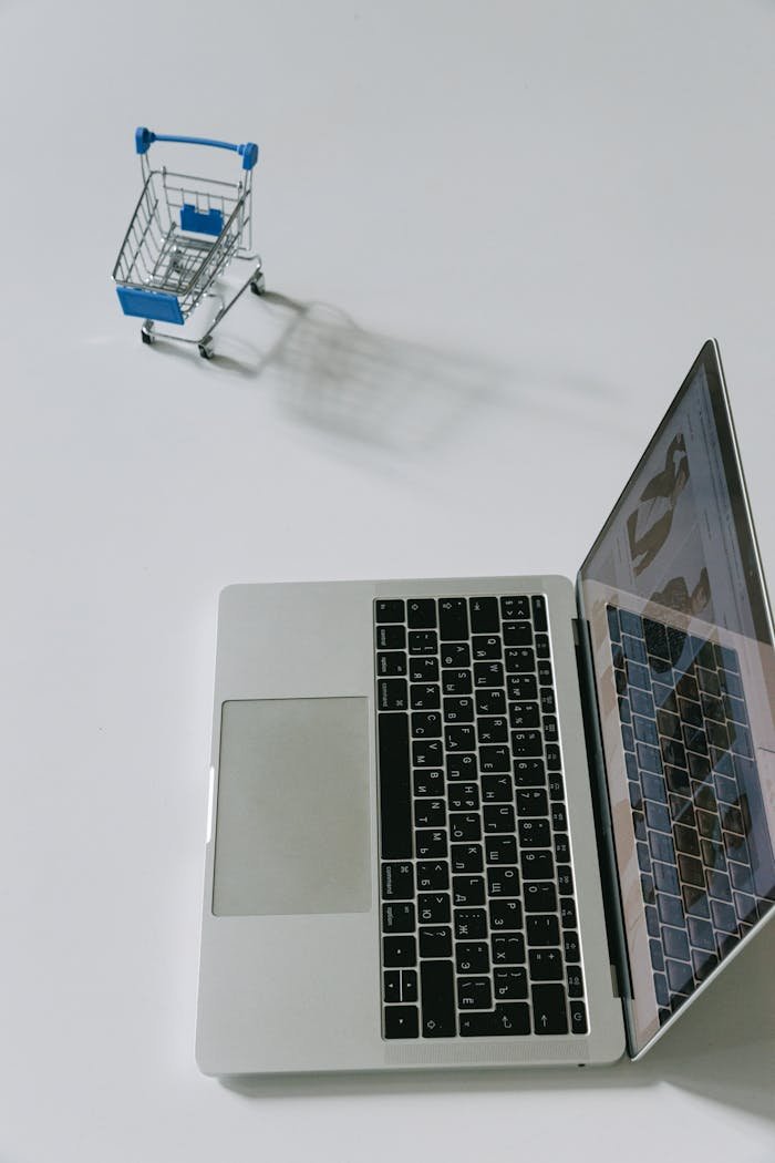 services-03 Minimalist scene of a laptop beside a miniature shopping cart symbolizing online shopping.